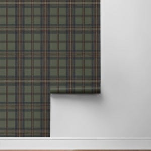 May include: A roll of wallpaper with a green, brown, and navy blue plaid pattern. The wallpaper is partially unrolled, revealing the pattern against a white wall and wooden floor.