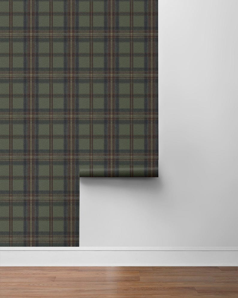 May include: A roll of wallpaper with a green, brown, and navy blue plaid pattern. The wallpaper is partially unrolled, revealing the pattern against a white wall and wooden floor.