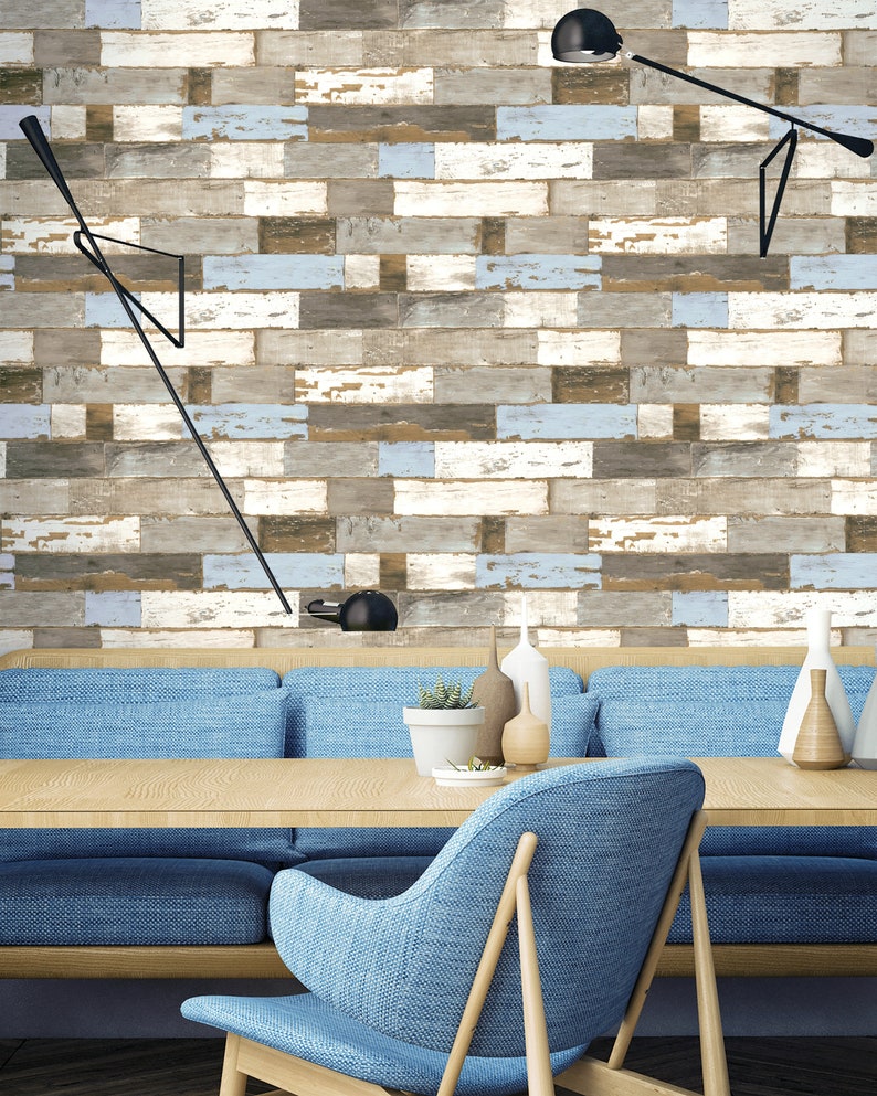 May include: A blue sofa and chair with wooden legs sit in front of a wall with a wood plank wallpaper design. The wall is decorated with two black lamps.