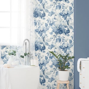 May include: A white bathroom with a white bathtub, a white vanity with drawers, and a white plant stand with a green plant. The walls are covered in a blue and white floral wallpaper.