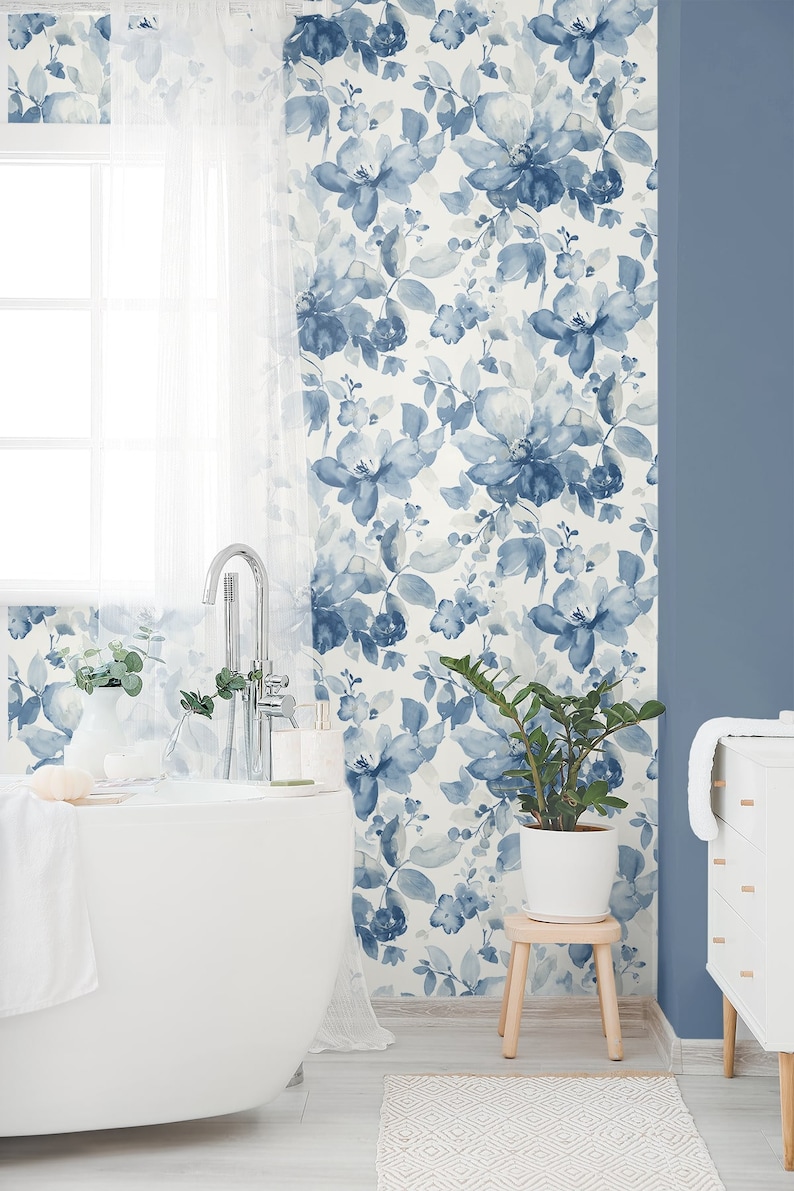 May include: A white bathroom with a white bathtub, a white vanity with drawers, and a white plant stand with a green plant. The walls are covered in a blue and white floral wallpaper.