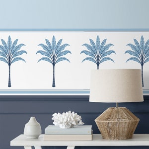 May include: A blue and white wallpaper border with a repeating pattern of palm trees. The border is shown on a wall with a blue lamp and a white vase on a white table.
