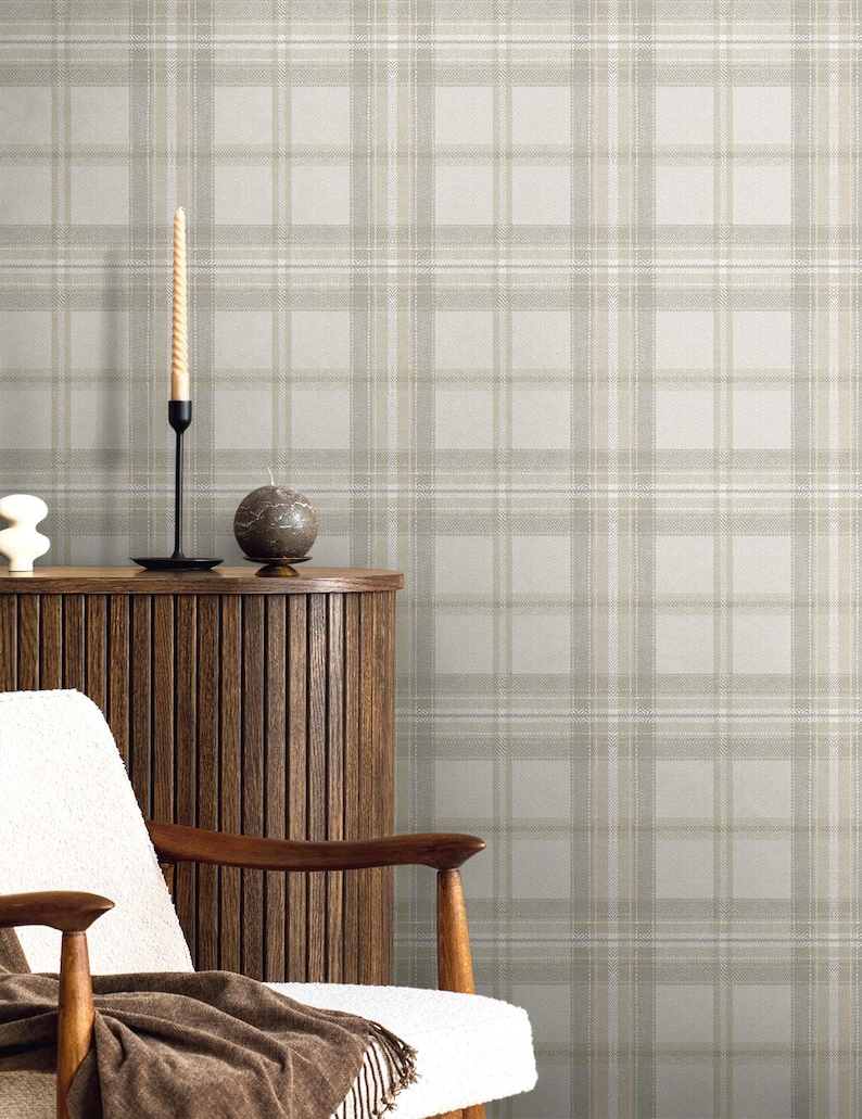 May include: A neutral-toned interior scene featuring a plaid wallpaper backdrop. A wooden cabinet, a white chair with wooden arms, and a brown throw blanket are in the foreground. A tall, spiral candle and a round candle sit on the cabinet.