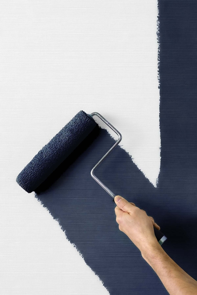 May include: A hand holds a paint roller, painting a dark blue line on a white wall. The roller is partially covered in blue paint, and the line is slightly uneven.