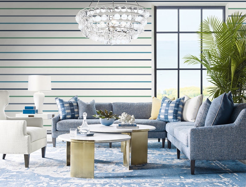 Puede incluir: Un sal&oacute;n moderno con decoraci&oacute;n azul y blanca. Cuenta con un sof&aacute; azul, cojines estampados y una mesa de centro redonda con patas doradas. Una gran ventana ofrece vistas al exterior y una l&aacute;mpara de ara&ntilde;a cuelga del techo.