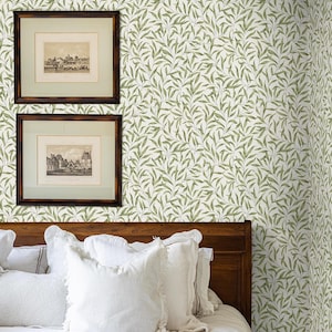 May include: A bedroom scene featuring a wooden bed frame, white bedding, and decorative pillows. The walls are covered in a green and white leaf pattern wallpaper. Two framed landscape prints hang above the bed, adding a touch of art.