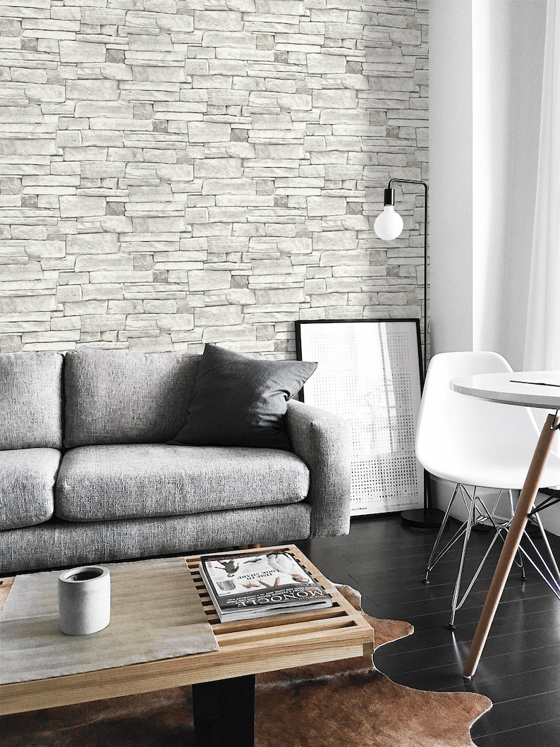 May include: A gray sofa with a magazine on a wooden coffee table in front of a white brick wall. A white chair and a floor lamp are in the background.
