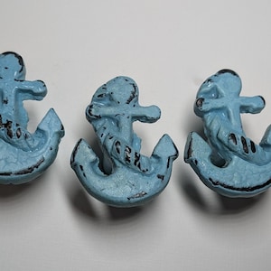 May include: Three light blue anchor-shaped decorative knobs with a distressed finish. The knobs have a mermaid design and black accents. Nautical-themed hardware for drawers or cabinets.