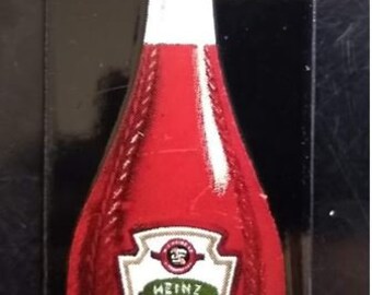 May include: A red Heinz Tomato Ketchup bottle with a white cap and label. The label reads "Heinz Tomato Ketchup" in a white and green design. The bottle is set against a black background.