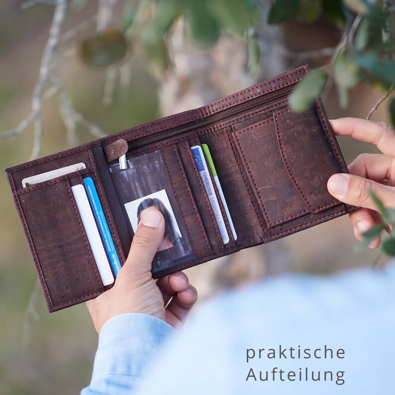 May include: A brown leather wallet with a zipper closure and multiple card slots. The wallet is open and has a clear plastic window for an ID card. The text "praktische Aufteilung" is visible at the bottom of the image.
