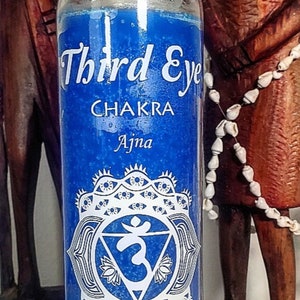 May include: A blue Third Eye Chakra candle in a glass jar. The candle has white text that reads "Third Eye Chakra Ajna" and a detailed white graphic. The bottom of the candle reads "Clear Perspective & Intuition, I Perceive."