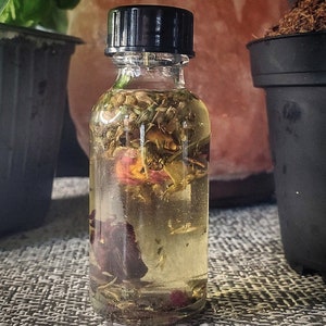 May include: A clear glass bottle with a black lid filled with a yellow liquid and dried flowers and herbs.