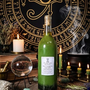 Puede incluir: Una botella llena de líquido verde con tapón de corcho, etiquetada como "Divinity Crystals Electromagnetic Field Bath". La botella está sobre una superficie de madera con velas, cristales y una bola de cristal. Un tapiz negro con símbolos dorados está en el fondo.