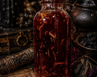 May include: A clear glass bottle with a black cap filled with a dark red liquid and botanical inclusions. Beside the bottle lies a rectangular parchment card printed with the text BAD LUCK EVIL EYE CURSES UNDO & REVERSE and an eye icon.