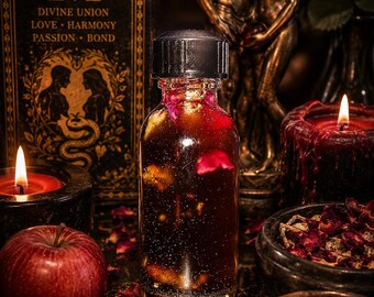 May include: A clear glass bottle with a black screw cap containing a dark amber liquid with visible red rose petals and small botanical pieces suspended inside, creating a textured appearance within the cylindrical container.
