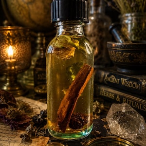 May include: A clear glass bottle with a black cap containing a golden liquid, a cinnamon stick, and dried botanical elements. The bottle is filled with oil and submerged plant matter, showcasing a cylindrical shape and a smooth, transparent surface.