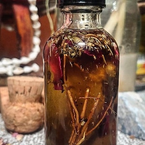 Könnte beinhalten: Eine klare Glasflasche mit schwarzem Deckel, gefüllt mit einer braunen Flüssigkeit und getrockneten Kräutern und Blumen. Die Flasche steht auf einer strukturierten Oberfläche.
