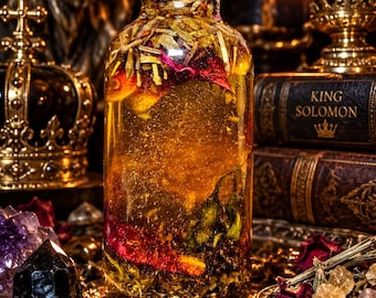 May include: A clear glass bottle with a black cap filled with golden liquid, dried flower petals, and herbs. The bottle contains visible botanical elements suspended in the oil, creating a textured appearance within the transparent container.