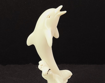 May include: A white porcelain dolphin figurine leaping out of the water. The dolphin is detailed with gold accents and is set on a base with waves.
