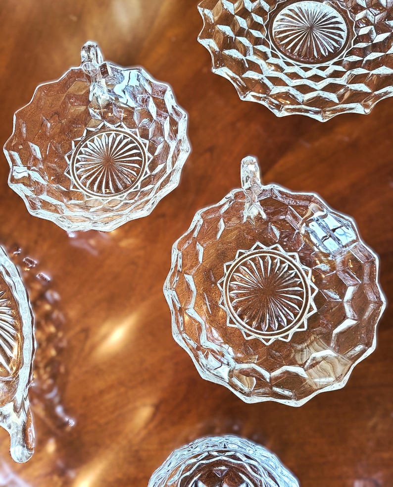 K&ouml;nnte beinhalten: Satz mit vier klaren Glasschalen mit einem Diamantenmuster und einem Sternendesign in der Mitte. Jede Schale hat einen Griff.