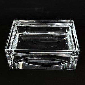 May include: A clear, rectangular glass box with a lid. The container features thick, transparent walls and a smooth, polished surface. The lid sits flush on the base, creating a seamless, unified appearance with sharp, defined edges and corners.