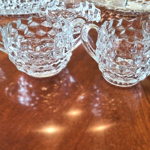 K&ouml;nnte beinhalten: Zwei klare Glask&auml;nnchen mit Diamantenmuster. Die K&auml;nnchen haben einen Henkel an einer Seite und stehen auf einer Holzoberfl&auml;che.