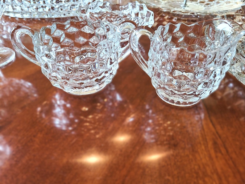 K&ouml;nnte beinhalten: Zwei klare Glask&auml;nnchen mit Diamantenmuster. Die K&auml;nnchen haben einen Henkel an einer Seite und stehen auf einer Holzoberfl&auml;che.