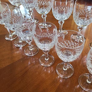 May include: A set of 10 clear crystal wine glasses with a diamond pattern. The glasses are arranged on a wooden table.