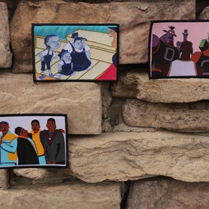 May include: Three embroidered patches featuring cartoon characters. One patch depicts a group of people, another shows a group of aliens, and the third shows a family. Each patch has a black border and is mounted on a stone wall.