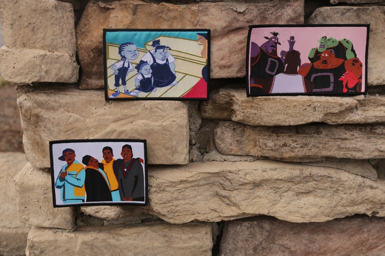 May include: Three embroidered patches featuring cartoon characters. One patch depicts a group of people, another shows a group of aliens, and the third shows a family. Each patch has a black border and is mounted on a stone wall.