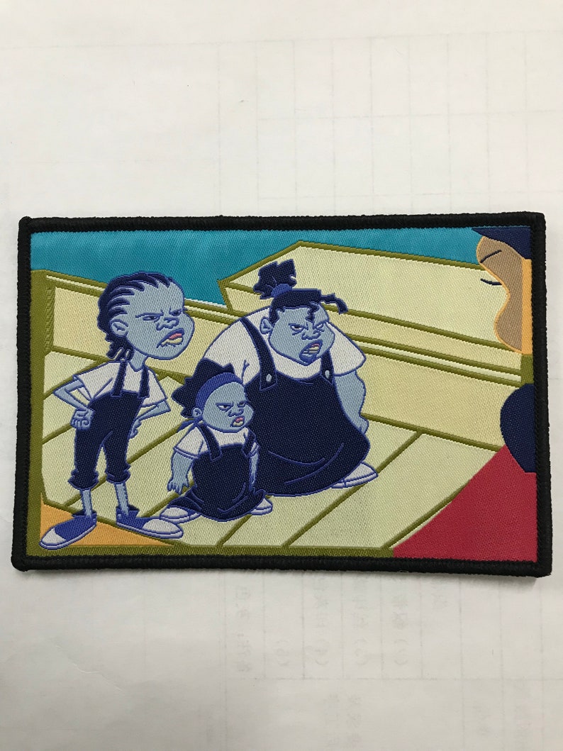May include: Embroidered patch featuring a cartoon scene with three characters in blue overalls and a stern expression. The background has a light blue sky and a beige floor. The patch is bordered with black.