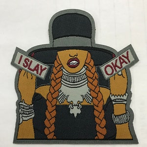 May include: Embroidered iron-on patch featuring a woman with long braids wearing a black hat and a black dress. The woman is holding two signs that say "I SLAY" and "OKAY".