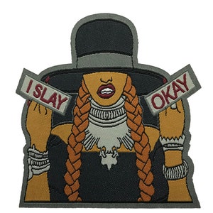 Peut inclure: Patch thermocollant brodé représentant une femme de dessin animé avec de longues tresses portant un chapeau noir et une robe noire. La femme tient deux pancartes qui disent "I SLAY" et "OKAY".