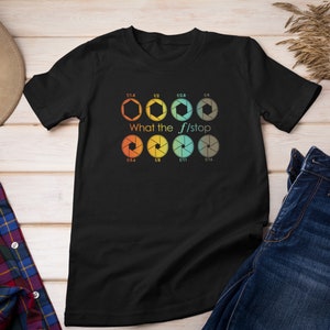 Op de afbeelding: Zwart T-shirt met een afbeelding van camera-diafragma-instellingen en de tekst "What the f/stop".