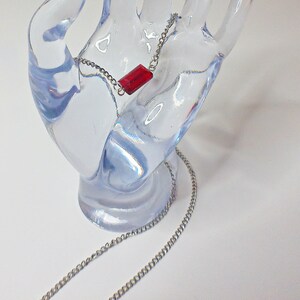 May include: A silver chain necklace with a red rectangular pendant.