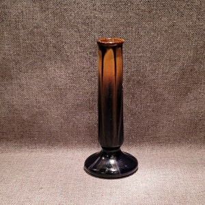 May include: A small, black and brown ceramic vase with a flared base. The vase has a glossy finish and a simple, elegant design.