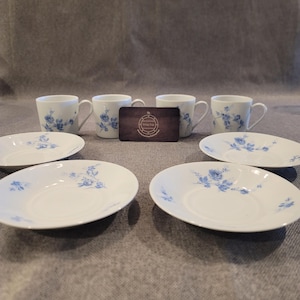 May include: A set of white porcelain teacups and saucers with a blue floral design. The set includes four teacups and four saucers. A wooden business card is placed between the teacups.