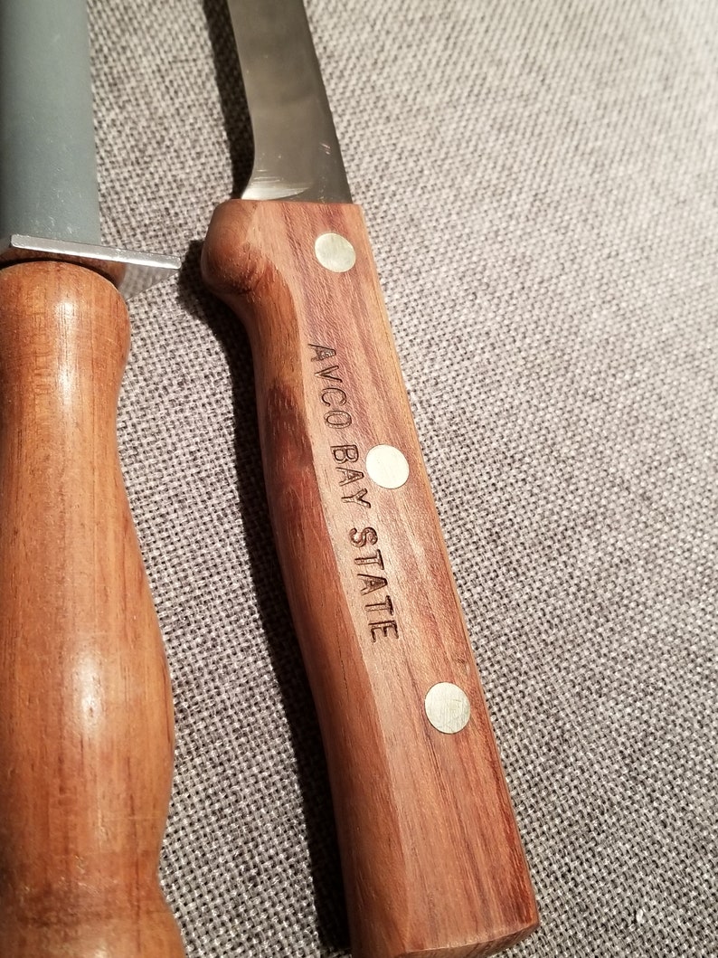 May include: A wooden handled knife with a stainless steel blade. The handle is engraved with the words "AVCO BAY STATE".