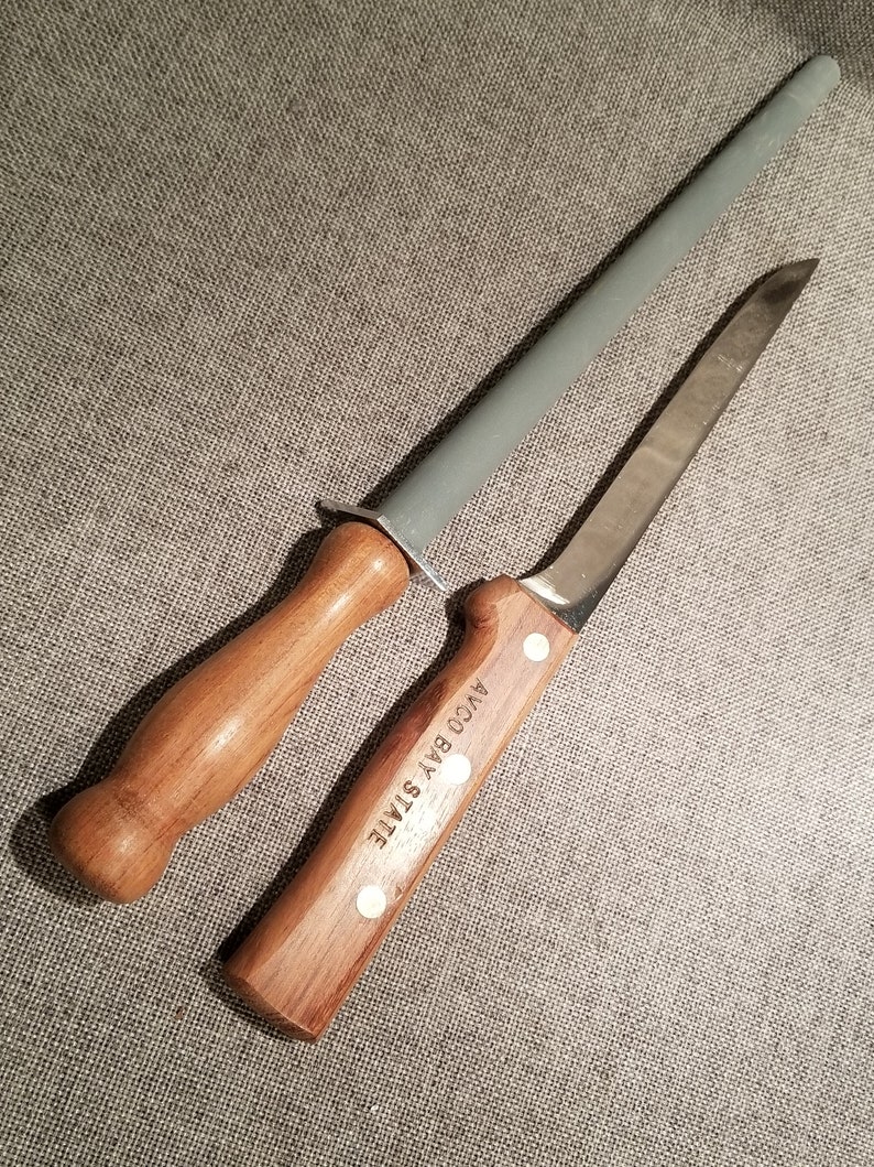 May include: A wooden handled knife with a stainless steel blade and a wooden handled sharpening steel. The knife handle has the text "AYCO BAY STATE" engraved on it.