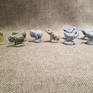 May include: A set of nine miniature figurines, including two women, two elephants, and five geese. The figurines are made of ceramic and painted in shades of blue, green, and gray.