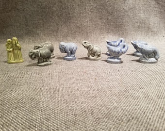 Könnte beinhalten: Ein Set mit neun Miniaturfiguren, darunter zwei Frauen, zwei Elefanten und fünf Gänse. Die Figuren sind aus Keramik und in Blautönen, Grün und Grau bemalt.
