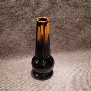 May include: A small, black and brown ceramic vase with a rounded base and a tall, narrow neck.