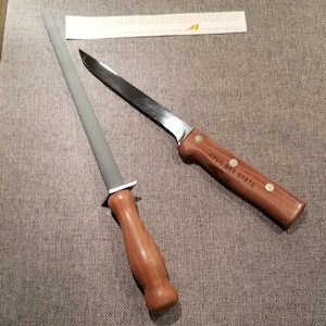 May include: A gray sharpening steel with a wooden handle and a silver knife with a wooden handle that says "W.R. CASE & SONS  BRADFORD, PA.  U.S.A.  O-BAY STATE"