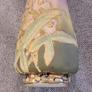 May include: A small, green and white ceramic vase with a floral design. The vase has a gold rim and a gold floral pattern. The vase is decorated with a white and gold floral design.