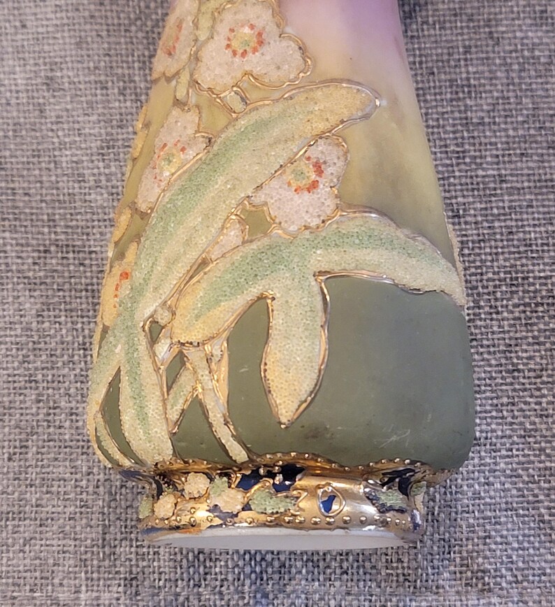 May include: A small, green and white ceramic vase with a floral design. The vase has a gold rim and a gold floral pattern. The vase is decorated with a white and gold floral design.