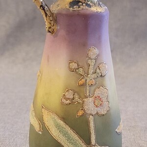 May include: A small, hand-painted porcelain pitcher with a gold handle and floral design. The pitcher is decorated with a green, yellow, and purple gradient and features a delicate floral motif with gold accents.