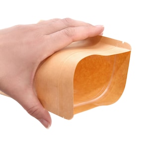 May include: A brown paper bag with a clear plastic window. The bag is open and the window is visible. The bag is being held by a hand.