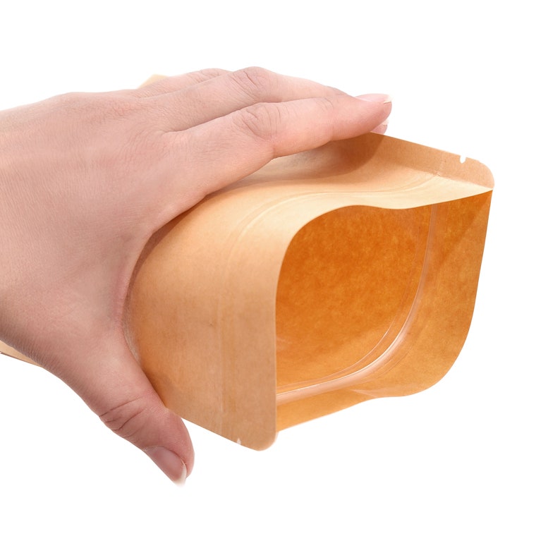 May include: A brown paper bag with a clear plastic window. The bag is open and the window is visible. The bag is being held by a hand.