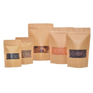 May include: Five brown paper bags with clear viewing windows, each filled with different types of food items. The bags have a zipper closure and are standing upright on a white background.