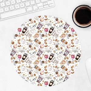 May include: Round white mousepad with a coffee-themed pattern. The design includes coffee cups, coffee beans, cupcakes, and the text "But first coffee" and "Latte". A keyboard, a cup of coffee, and a mouse are also visible.
